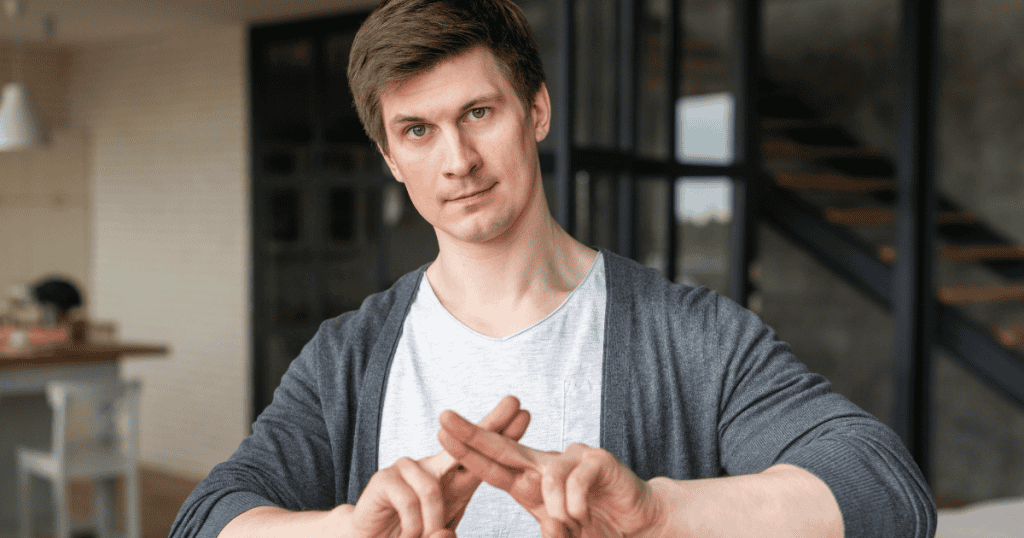 A man makes a firm "X" gesture with his fingers; the sharp motion conveys a non-verbal command that halts any further discussion.