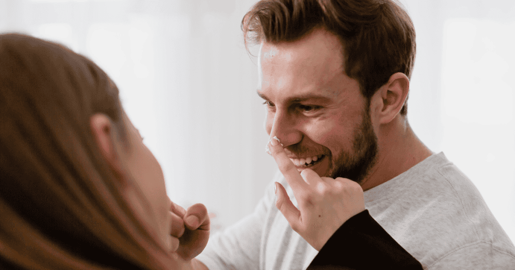 A woman playfully touches a manโs nose as he laughs, depicting the initial, effortless charm that marks the beginning of a complex journey.