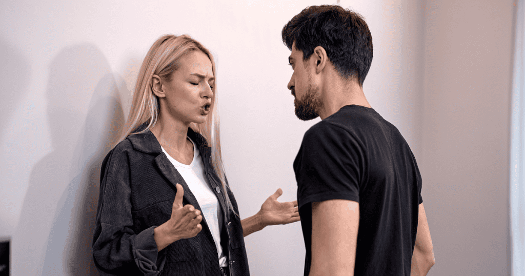 A woman speaks emphatically toward a man leaning against a wall, illustrating a tense moment where personal truths are being redirected.