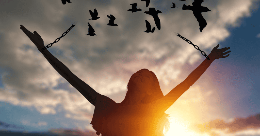 A woman raises her arms toward a sunset as chains break and turn into birds, capturing the moment an epiphany leads to the release of a heavy burden.