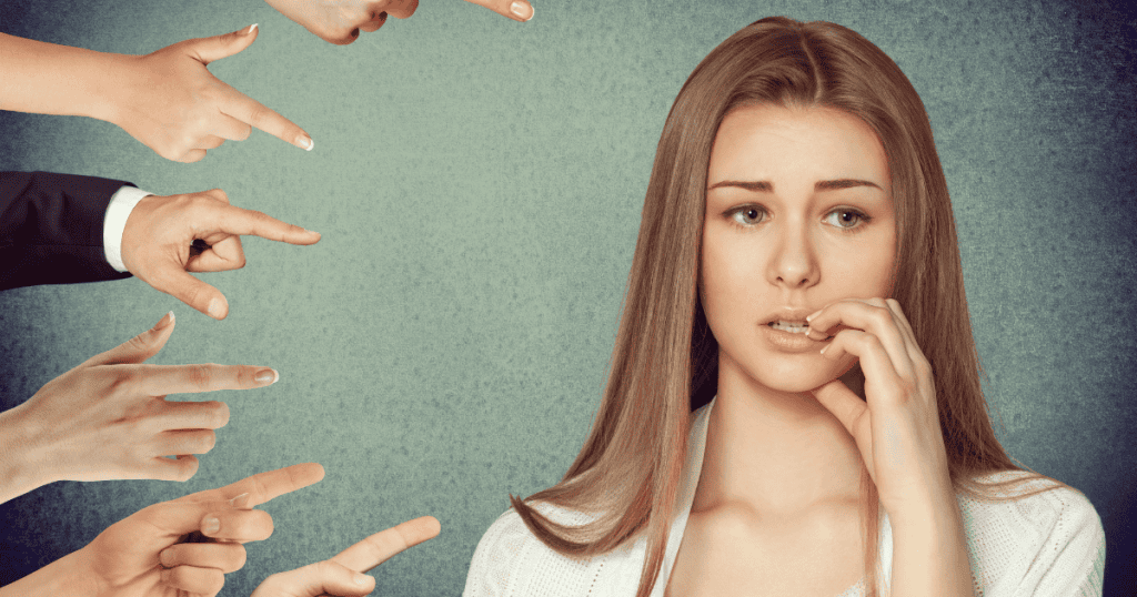 A woman bites her nails as multiple hands point accusingly at her; her anxious expression highlights the weight of external blame.