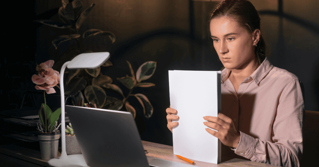 A woman intently reviewing a thick stack of white papers under a desk lamp, anchoring herself in a verifiable paper trail.