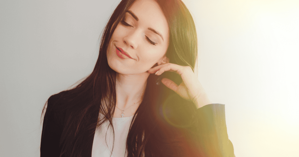 A woman tilts her head back with a serene, knowing smile and closed eyes, finally releasing the internal weight of a diminished self-perception.