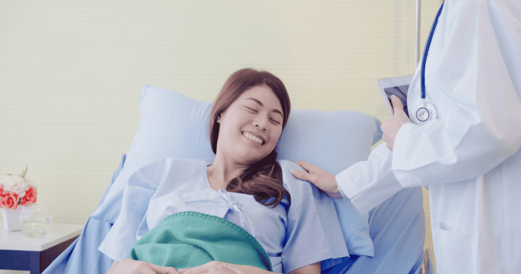 A woman smiles from a hospital bed as a doctor rests a hand on her shoulder, a moment of clinical care that highlights the absence of genuine support elsewhere.