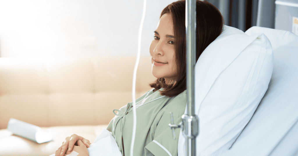 A patient looks off-camera with a faint, weary smile while hooked to an IV, reflecting a quiet resilience in a dynamic where her needs are never the priority.