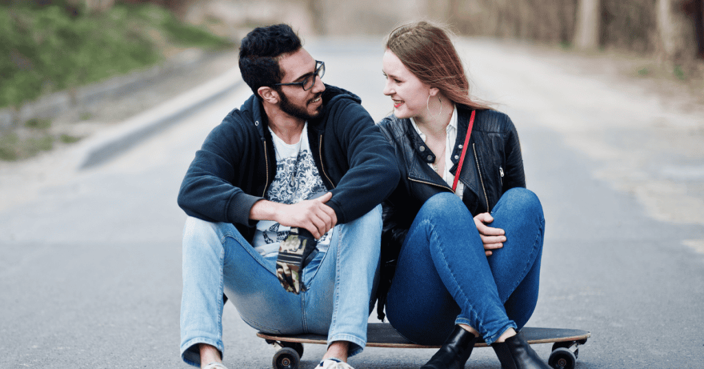 Two people sit together on a longboard in the middle of a road, showing a shift from being stuck in place to finding a shared path forward.
