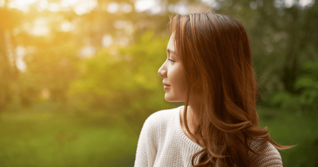 A woman gazes thoughtfully into a sunlit forest, capturing the internal peace that comes from choosing a more private path.