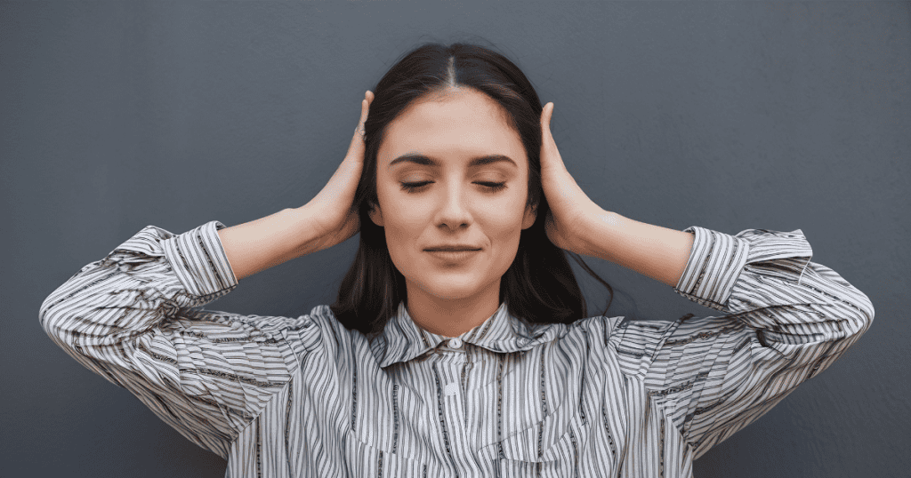 A woman closes her eyes and covers her ears with her hands, finding a sense of internal peace by tuning out the external noise.