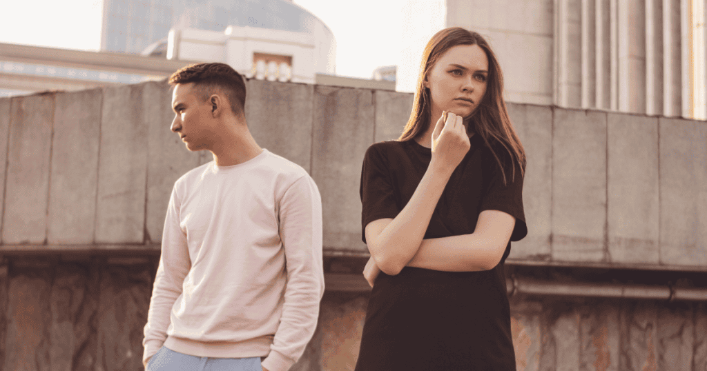 A man and woman stand back-to-back against a concrete ledge, emphasizing the newfound boundaries and distance required to protect oneโs peace.
