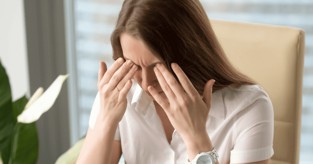 A woman at a desk presses her fingers against her closed eyes, demonstrating the quiet endurance required to outlast a grueling situation.