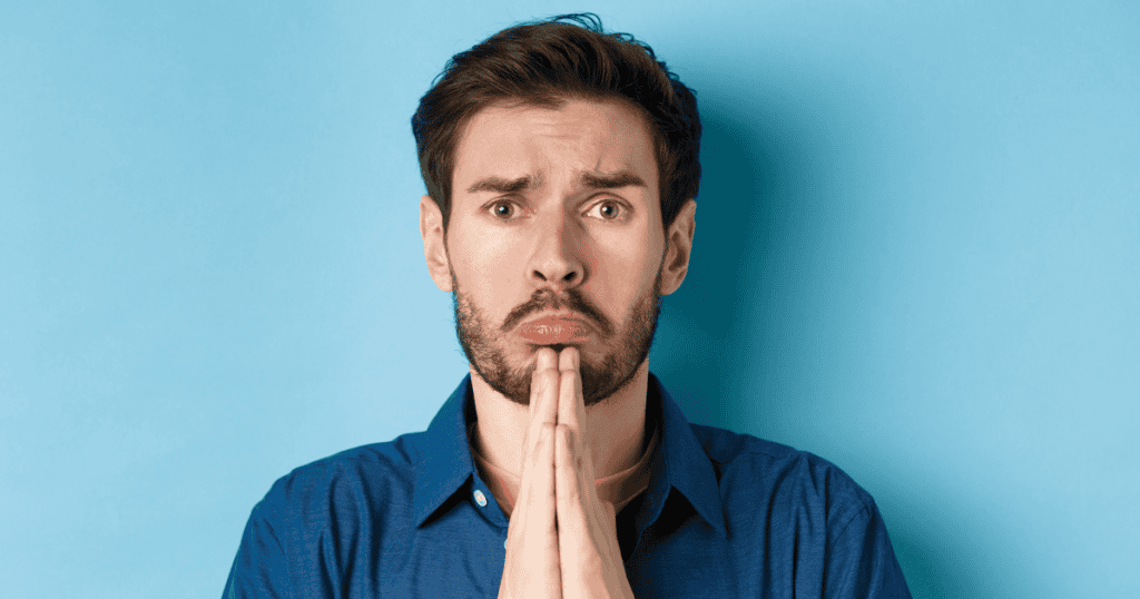 A man with an exaggerated pout holds his hands together in a pleading gesture, embodying a desperate attempt to regain favor.