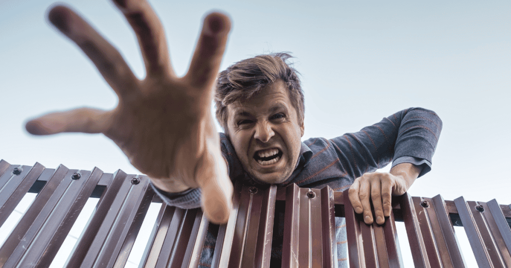 A furious man leans over a fence, reaching aggressively forward with an outstretched hand, illustrating the explosive and chaotic nature of a narcissist’s emotional breakdown.