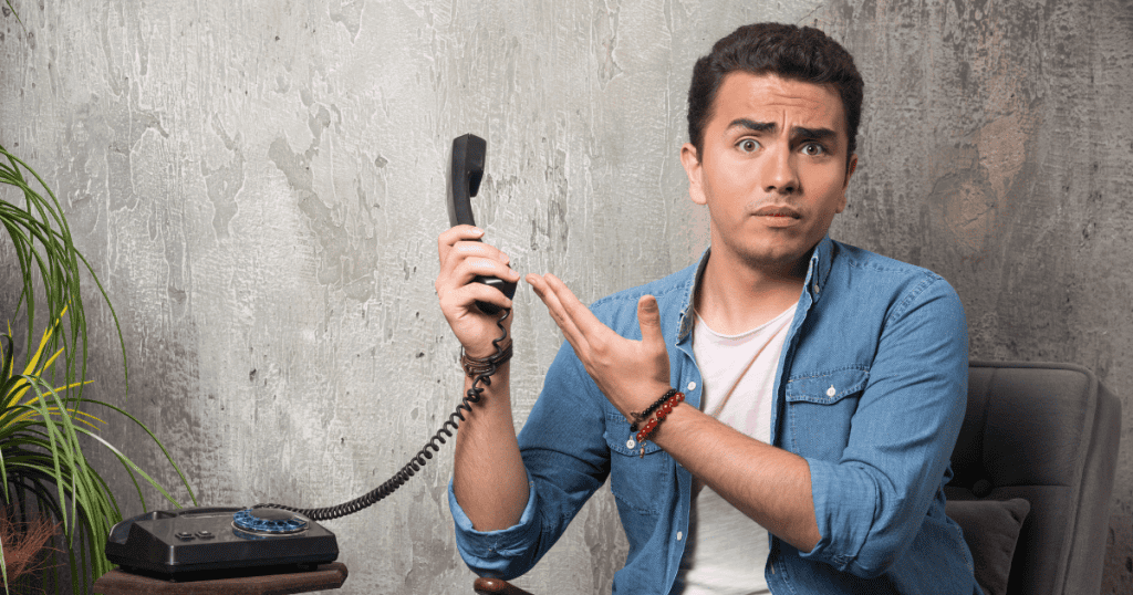 A man holds a vintage telephone receiver out with a confused, questioning gesture; his expression captures the frustration of a one-sided connection.