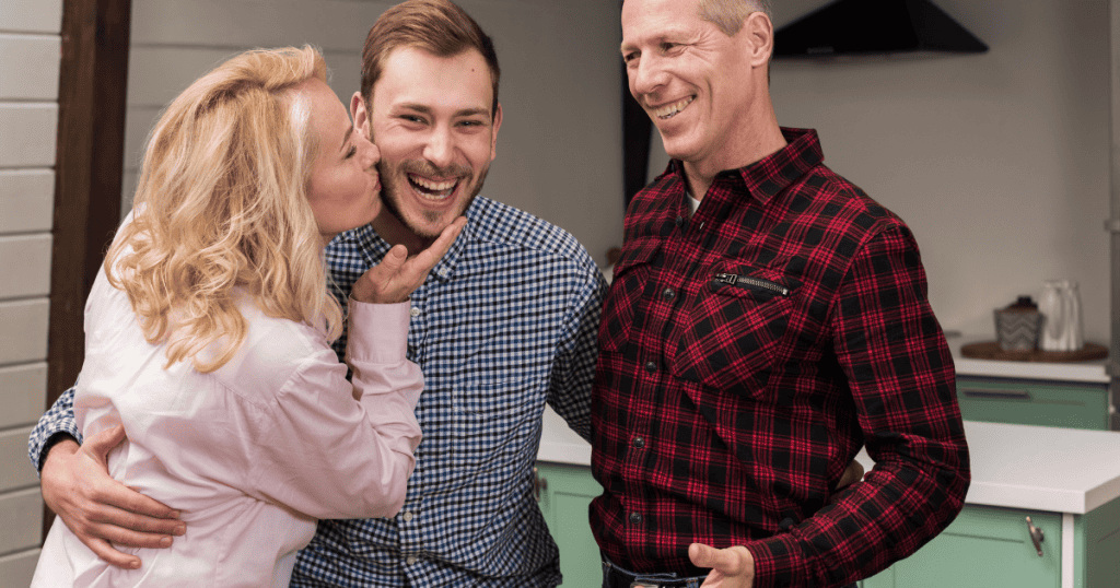 A woman kisses a laughing young man on the cheek while an older man watches with a wide smile, reflecting the complex dynamics of seeking place within a family circle.