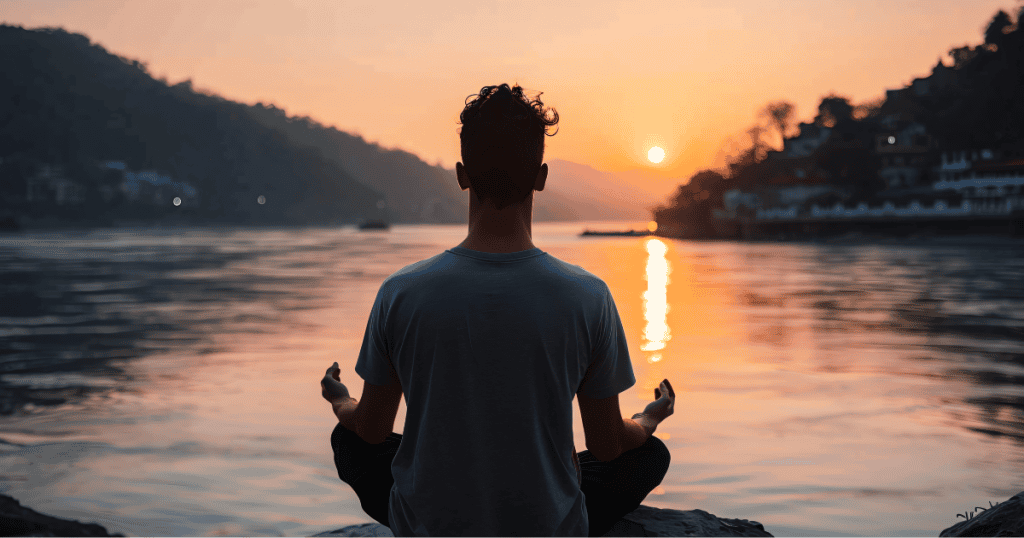A person meditates peacefully by a calm river at sunset, using a serene facade of mindfulness to silently assert dominance over their surroundings.