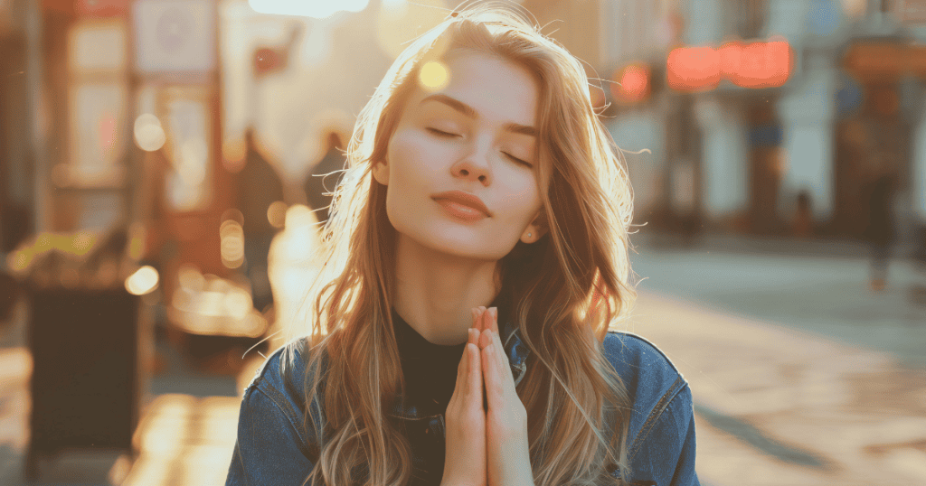 A woman stands in the soft glow of sunset with her eyes closed and hands clasped in prayer, capturing the quiet relief of a newfound clarity.