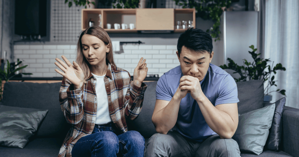 A man sits in somber silence on a couch while a woman beside him gestures dismissively, illustrating the heavy tension of a connection that has finally reached its breaking point.