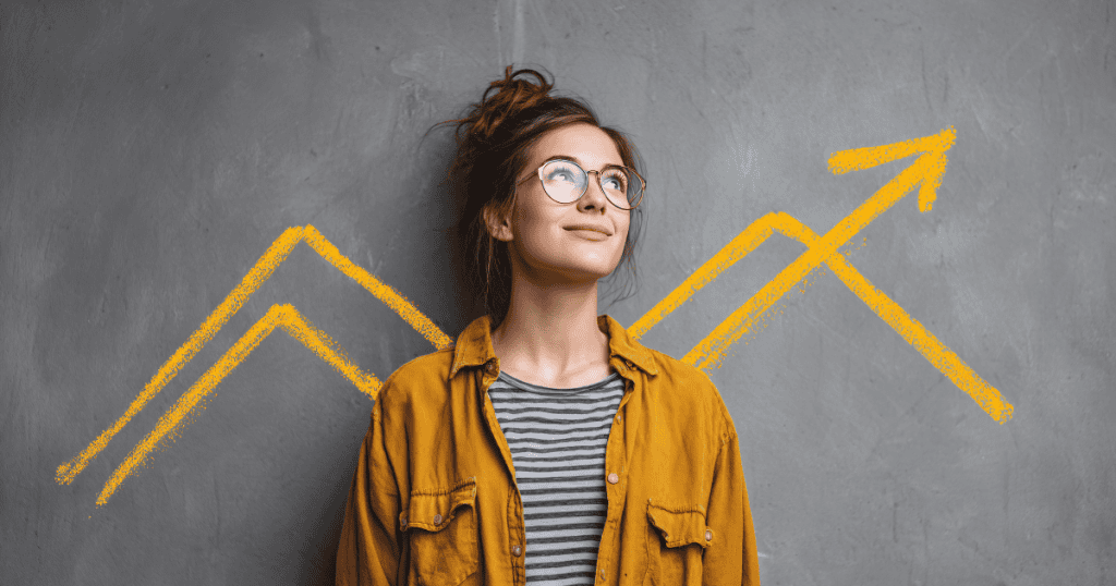 A young woman smiles upward in front of a gray wall marked with yellow upward-trending lines, reflecting an internal shift toward personal growth.