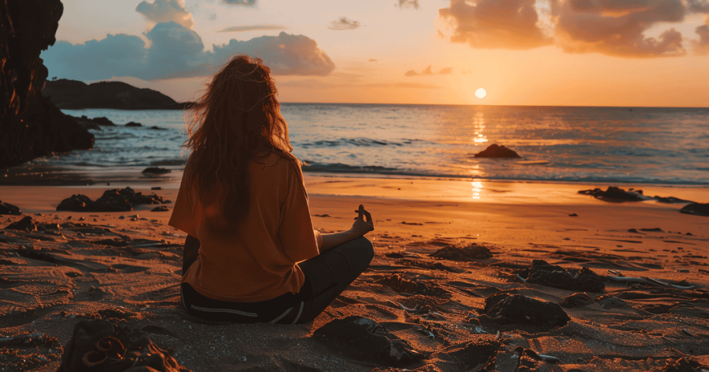 A woman sits in a meditative pose on a beach facing a vibrant sunset, signifying the internal peace found when external validation no longer carries weight.