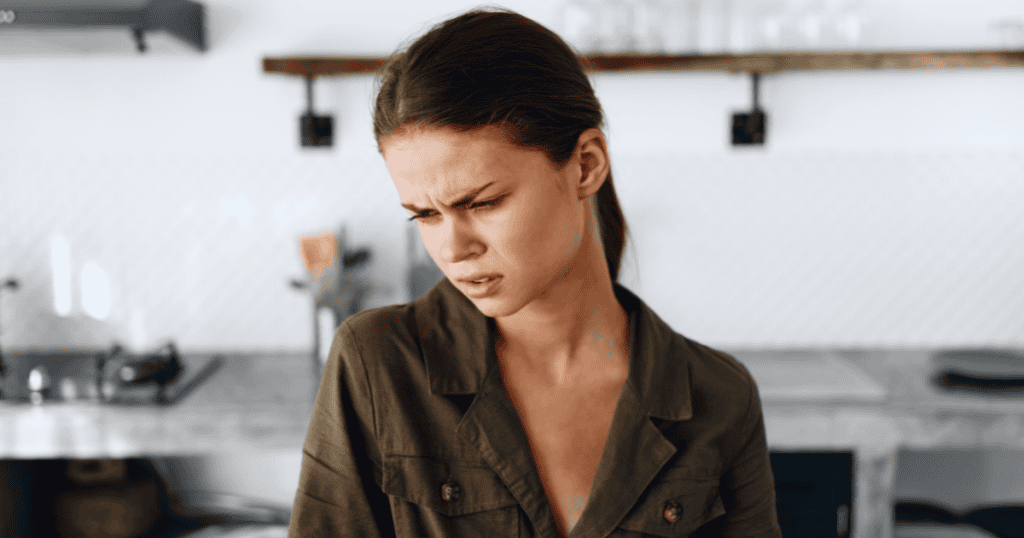 A woman in a kitchen wears a pained and conflicted facial expression, revealing a crack in a normally composed exterior.