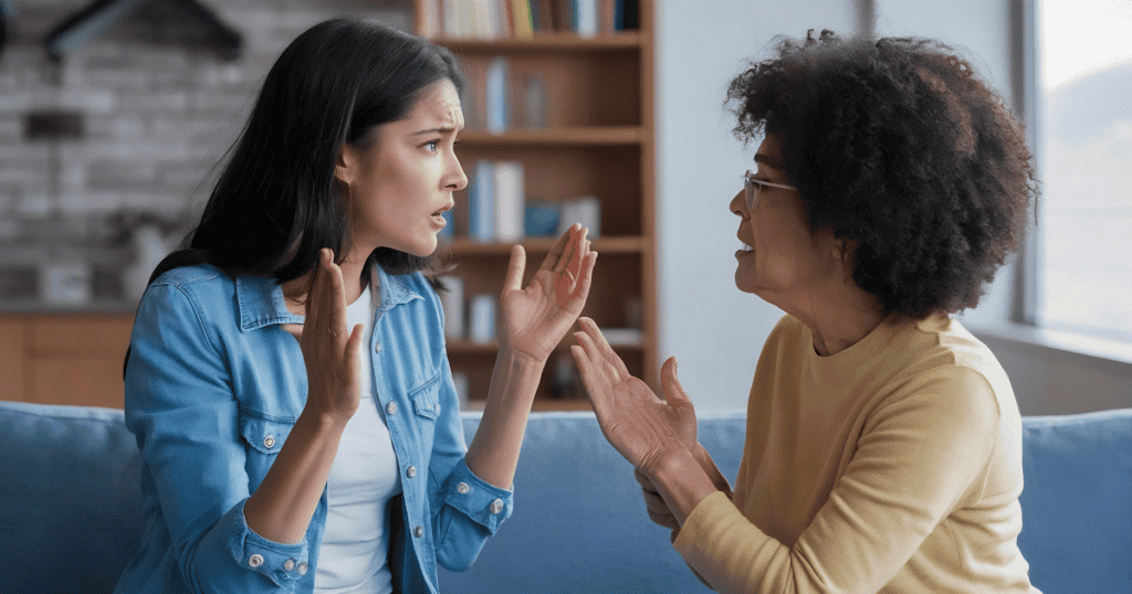 Two women engage in a heated, animated confrontation on a sofa, illustrating the visible friction that develops when communication styles consistently clash.