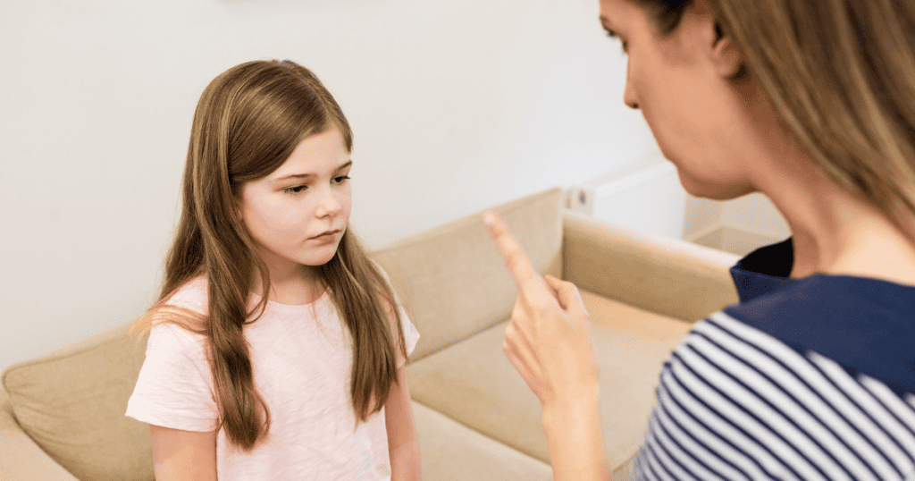 A young girl looks down somberly while an adult points a finger at her, capturing a moment where external authority begins to override internal voice.