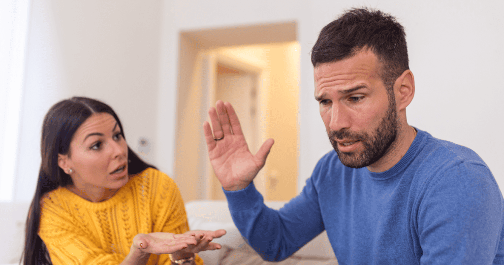 A man turns his head away and raises a hand in a dismissive gesture while a woman continues to speak, capturing a moment of self-preservation against an overwhelming dialogue.