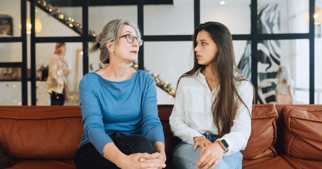 An older woman looks away thoughtfully while a younger woman watches her with a concerned, confused expression, highlighting the disconnect that occurs when social cues are missed.