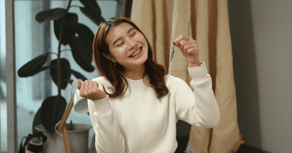 A smiling woman holds up a set of new keys with a look of triumph, marking a tangible milestone in reclaiming her personal agency.