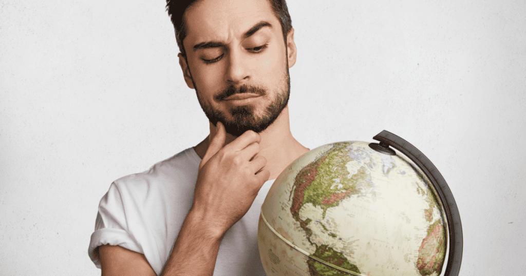 A man rubs his chin thoughtfully while looking down at a desk globe, contemplating how certain regions of the world compare in the context of large-scale behavioral data.