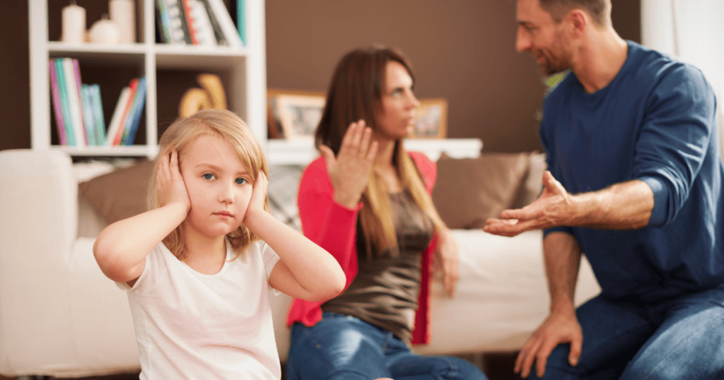 A child covers her ears while adults argue in the background, illustrating a deep-seated desire to distance oneself from loud or overbearing behavior.