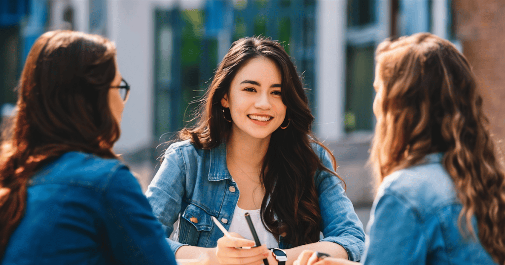 A woman smiles warmly at her friends while sitting at an outdoor table, maintaining a pleasant exterior that may mask the suppression of her own needs.