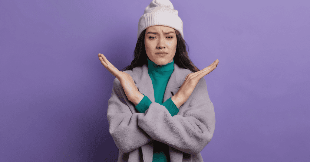 A woman in a winter hat crosses her arms in a firm "X" gesture, signaling a refusal to be swayed by outward emotional pleas.