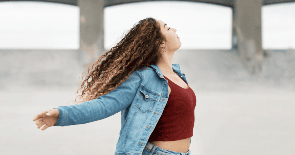 A woman stands with her eyes closed and arms outstretched to catch the breeze, embodying the sense of clarity and personal liberation found after gaining new understanding.