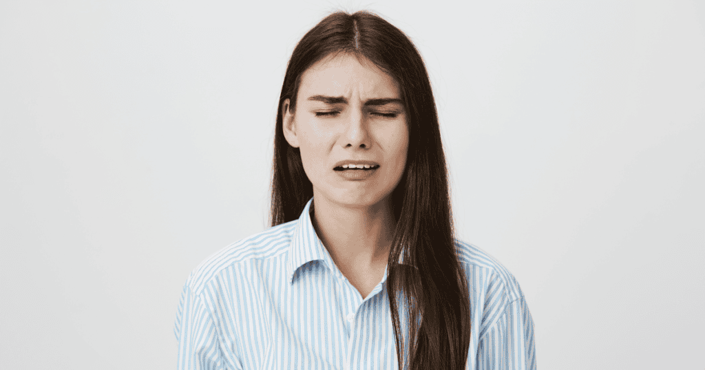 A woman winces with her eyes squeezed shut in a display of distress, illustrating how visceral reactions can effectively mirror genuine pain.