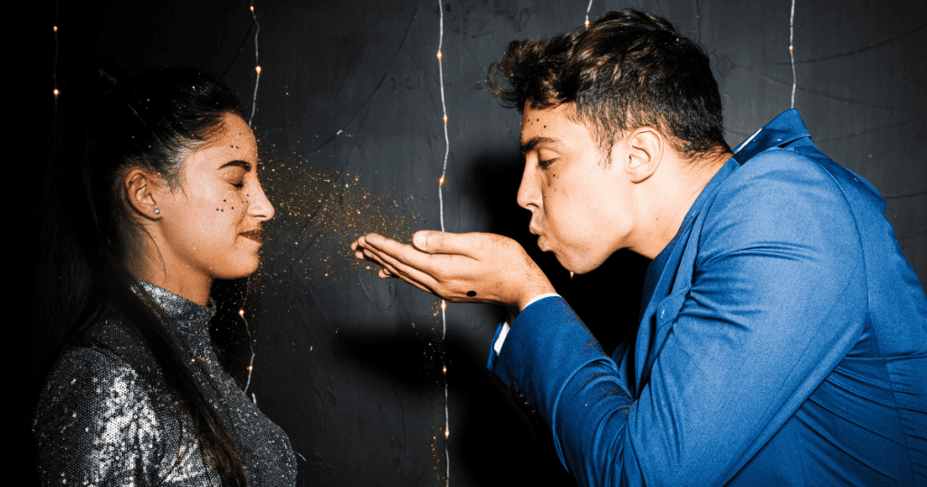 A man blows gold glitter into the face of a woman who keeps her eyes closed, a dazzling gesture that serves to temporarily obscure what is actually happening between them.