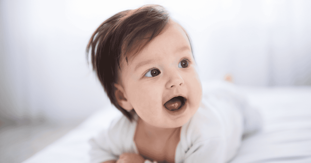 A bright-eyed infant lies on a white surface with an open-mouthed smile, capturing the initial stage before external expectations begin to shape a curated persona.