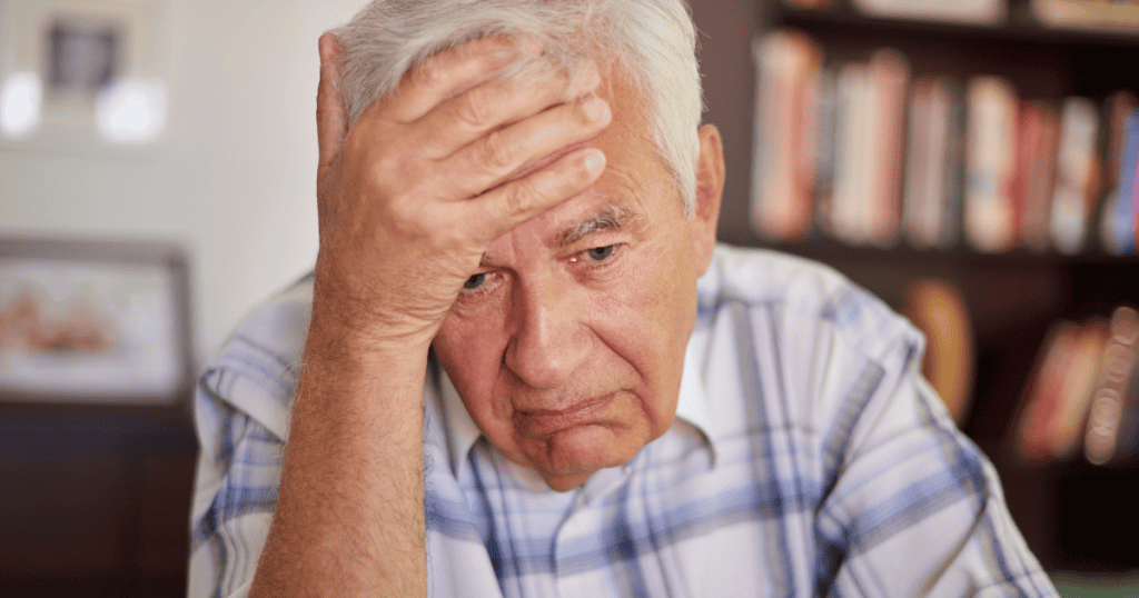 An elderly man rests his head heavily in his hand with a somber, downcast expression, representing the final stage where the long-held facade can no longer support itself.