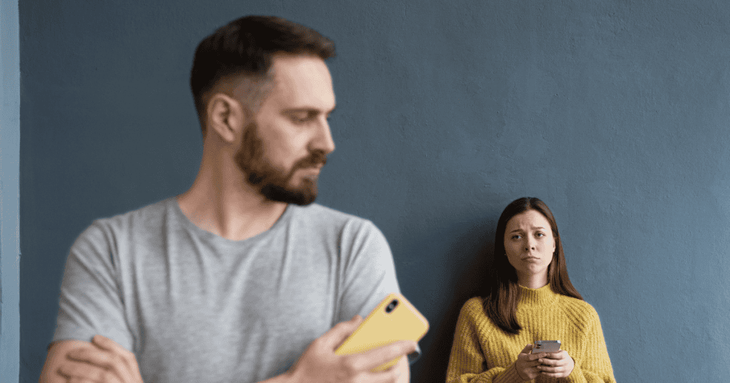 A man looks away while holding a phone as a woman watches him sadly, signaling a growing digital divide and a lack of presence.