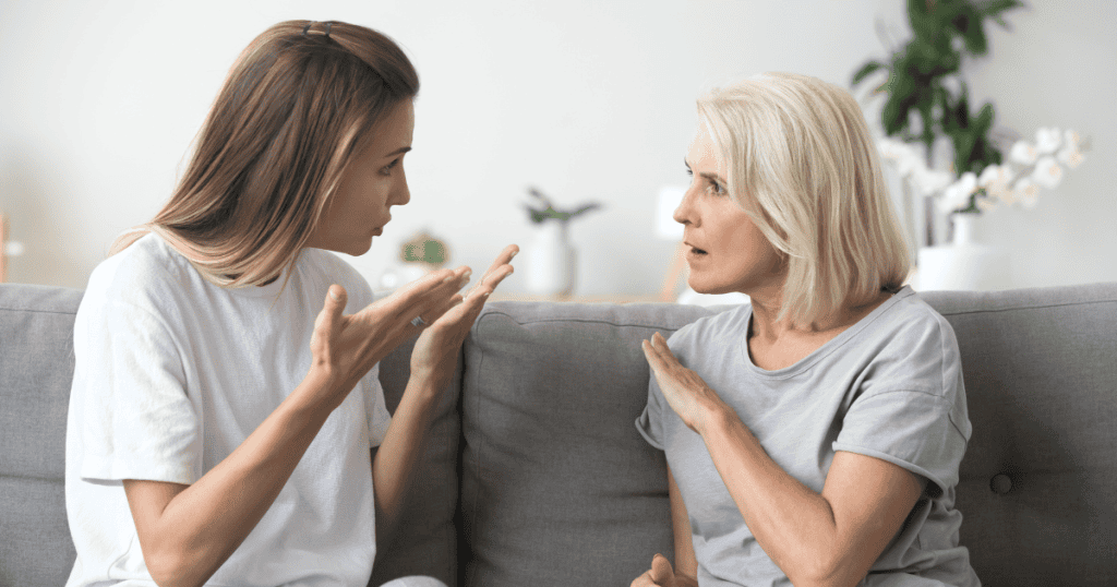 A younger woman speaks urgently with expressive hand movements while an older woman counters with an upright, defensive hand gesture, showcasing the friction that occurs when unyielding boundaries are first introduced.
