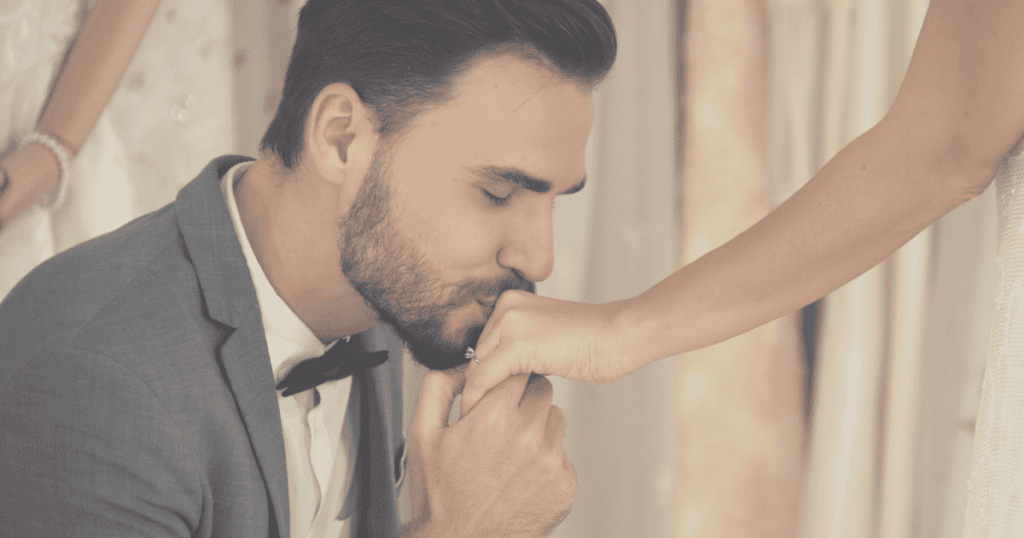 A groom tenderly kisses a bride’s hand during a ceremony, performing the ultimate gesture of a commitment he cannot internally sustain.