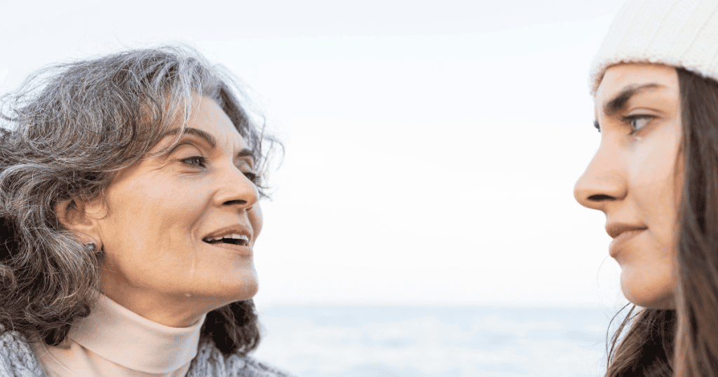 An older woman speaks intensely to a younger woman whose face is partially visible, a close-up encounter where the emotional weight is placed entirely on the person receiving the message.
