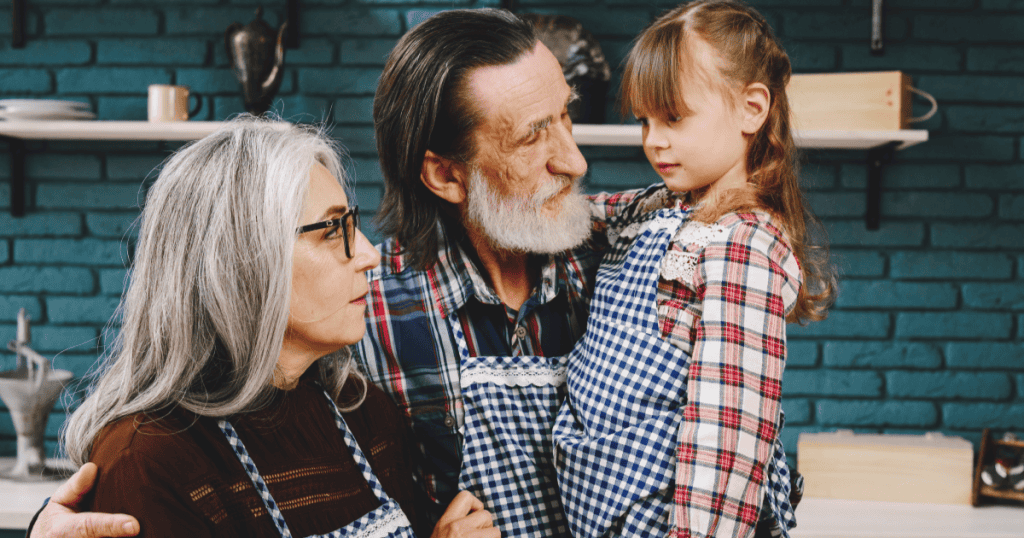 Grandparents holding their young granddaughter close in a warm-looking embrace, illustrating the deceptively affectionate surface under which a narcissistic grandparent can quietly instill harmful lessons in a child's mind.