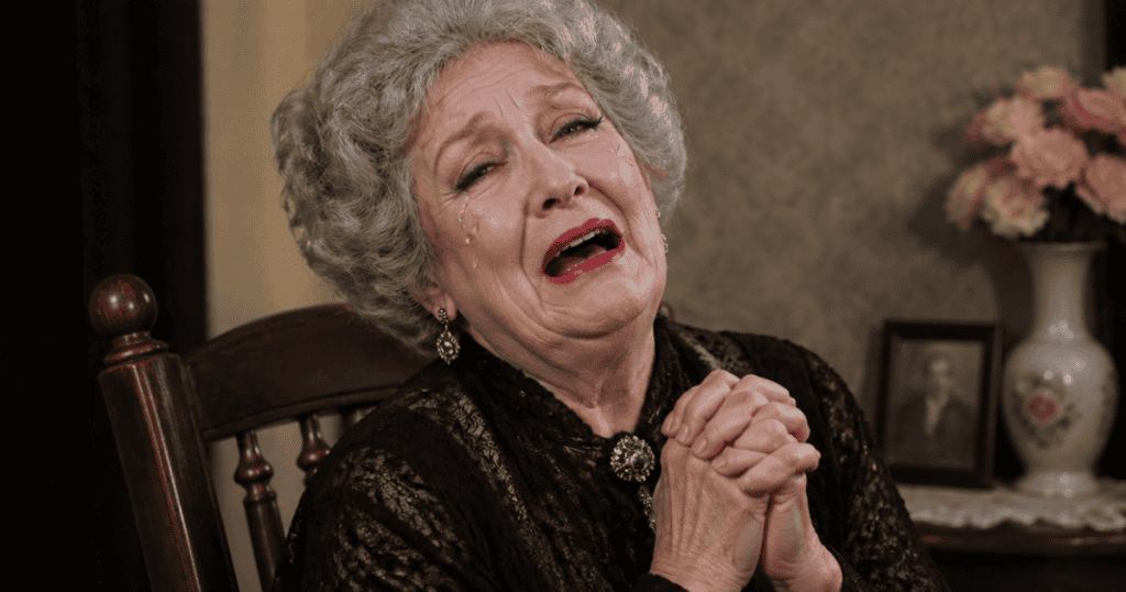 An elderly woman in a black lace dress sits with her hands tightly clasped in prayer while weeping with open-mouthed anguish, showcasing a highly dramatic presentation of personal suffering that instantly disarms any onlookers.