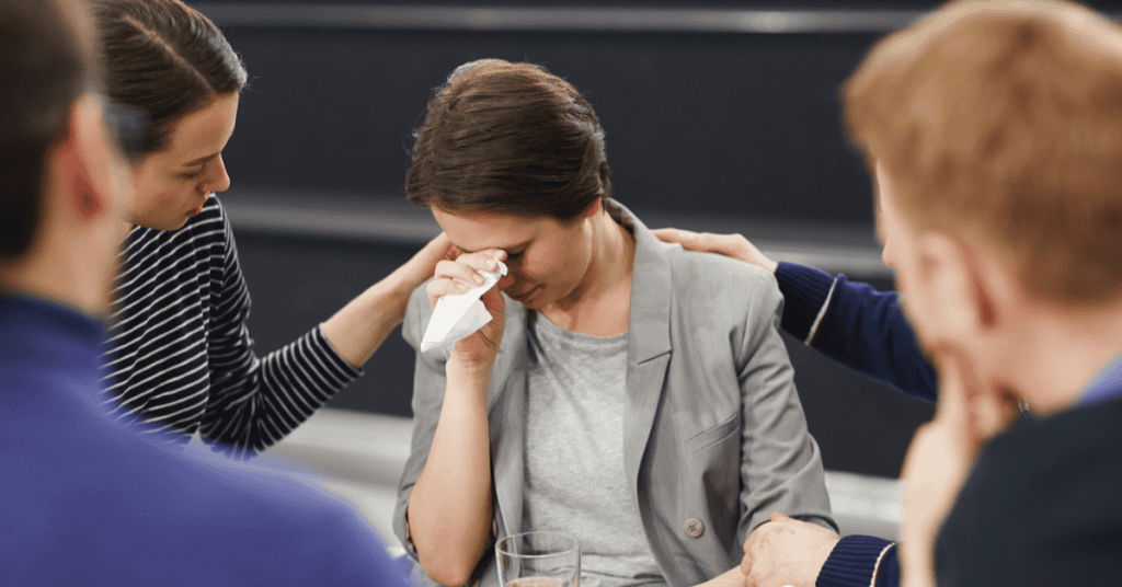 A woman crying and being comforted by those around her, illustrating how a female narcissist uses tears and the victim role to manipulate sympathy and rewrite the narrative in her favor.