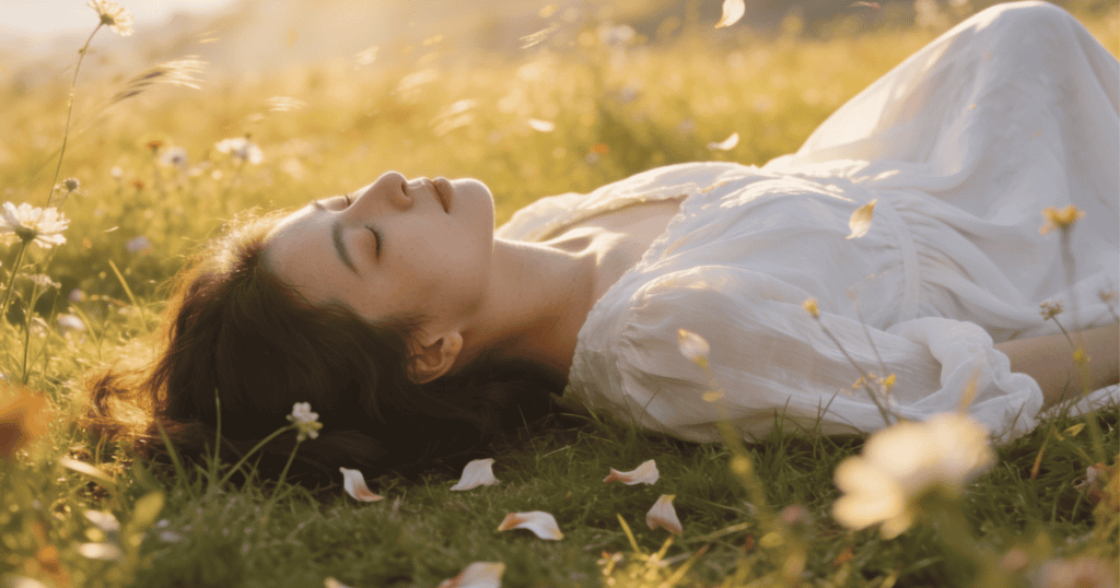 A woman lies peacefully on her back in a serene field of grass and white wildflowers as petals softly drift around her, beautifully capturing a quiet state of surrender and the liberating realization that none of it was ever yours to fix.
