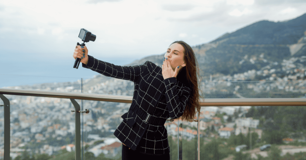 A woman blowing a kiss at her camera with a scenic cityscape behind her, reminding narcissistic abuse survivors that healing doesn't mean putting life on hold.