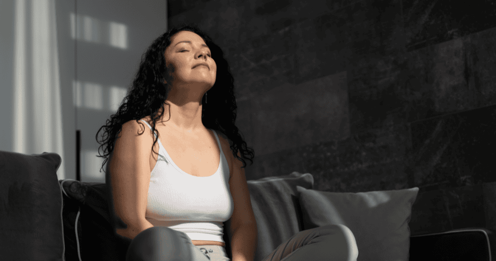 A woman sitting calmly in sunlight with eyes closed, embodying a healed survivor's ability to pause before reacting.