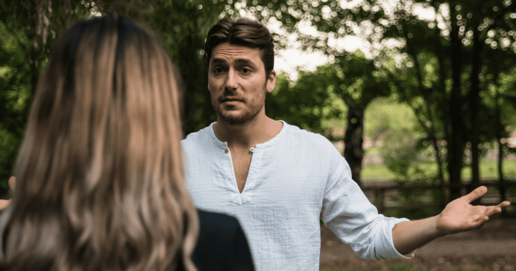 A man gestures with open hands and an incredulous expression toward a woman viewed from behind, illustrating the dismissive minimization used to invalidate another person's valid concerns.