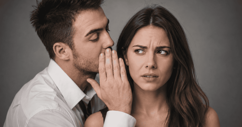 A man leans in close to whisper a secret while an uneasy woman glances sideways with deep suspicion, portraying the instinctive caution triggered by intrusive whispering campaigns.